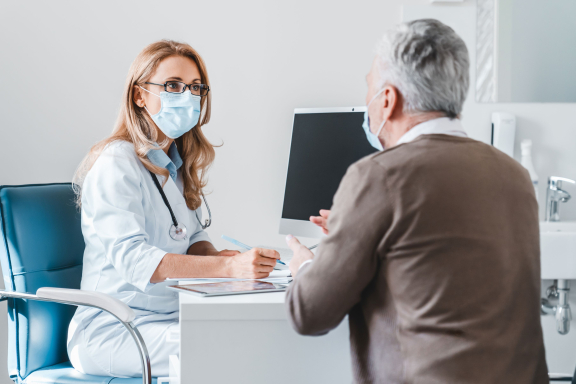 dokter in gesprek met patiënt mondmasker huisarts praten - iStock.com
