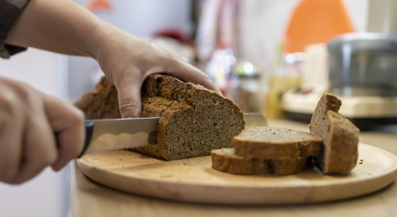 Persoon snijdt een snede van een volkorenbrood - iStockphoto