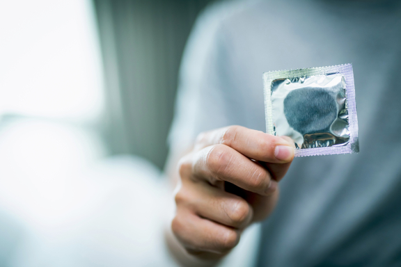 Man houdt condoom vast, hiv-virus - iStockphoto